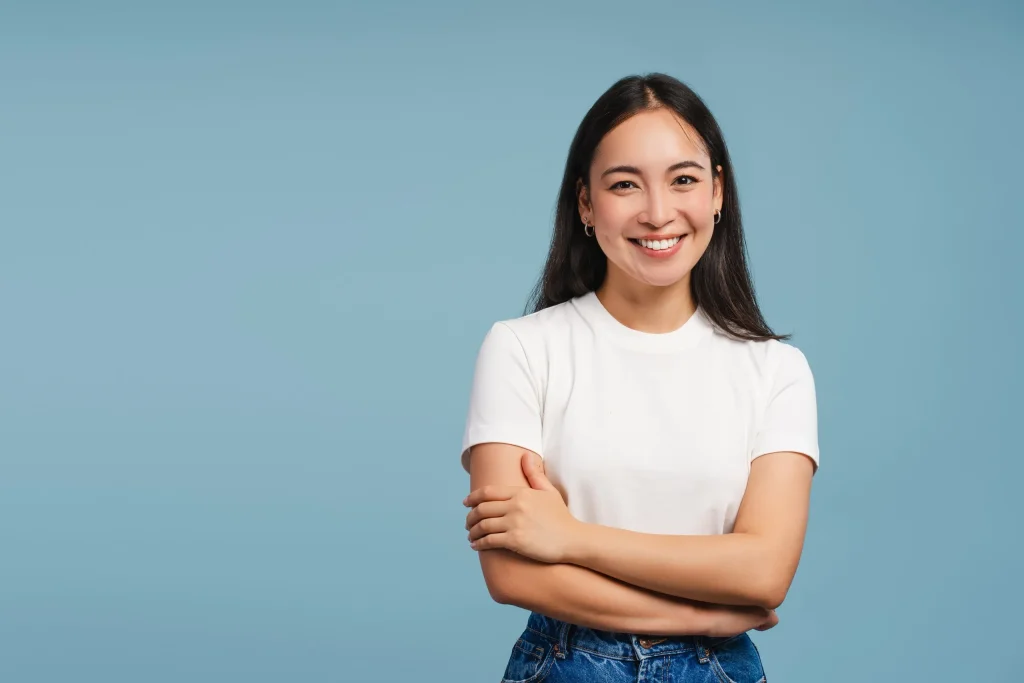 A smiling woman standing with her arms folded against a plain blue background.