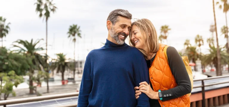 Smiling middle-aged couple embracing on a palm-lined waterfront promenade